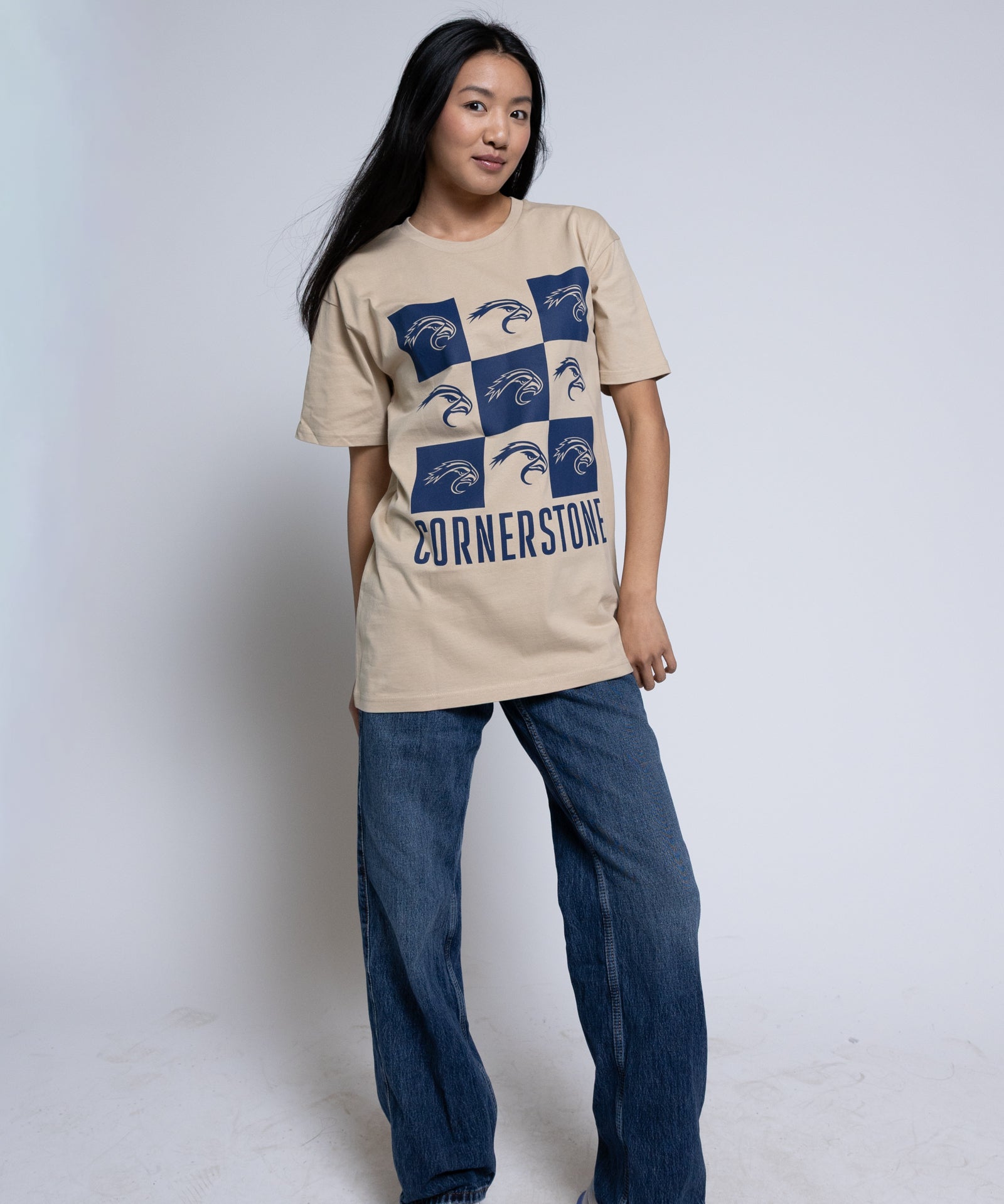 Woman wearing a beige t-shirt with a blue mascot checkered design and 'Cornerstone' text.