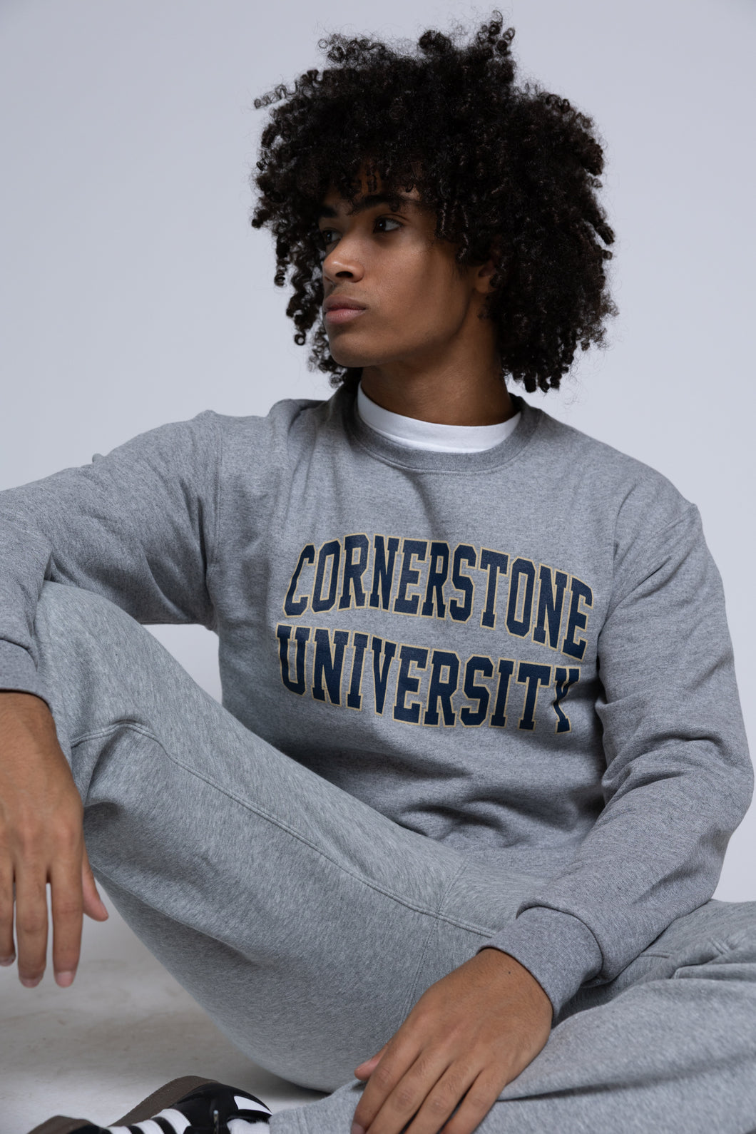 Person wearing a gray 'Cornerstone University' crew sweatshirt sitting on a white background