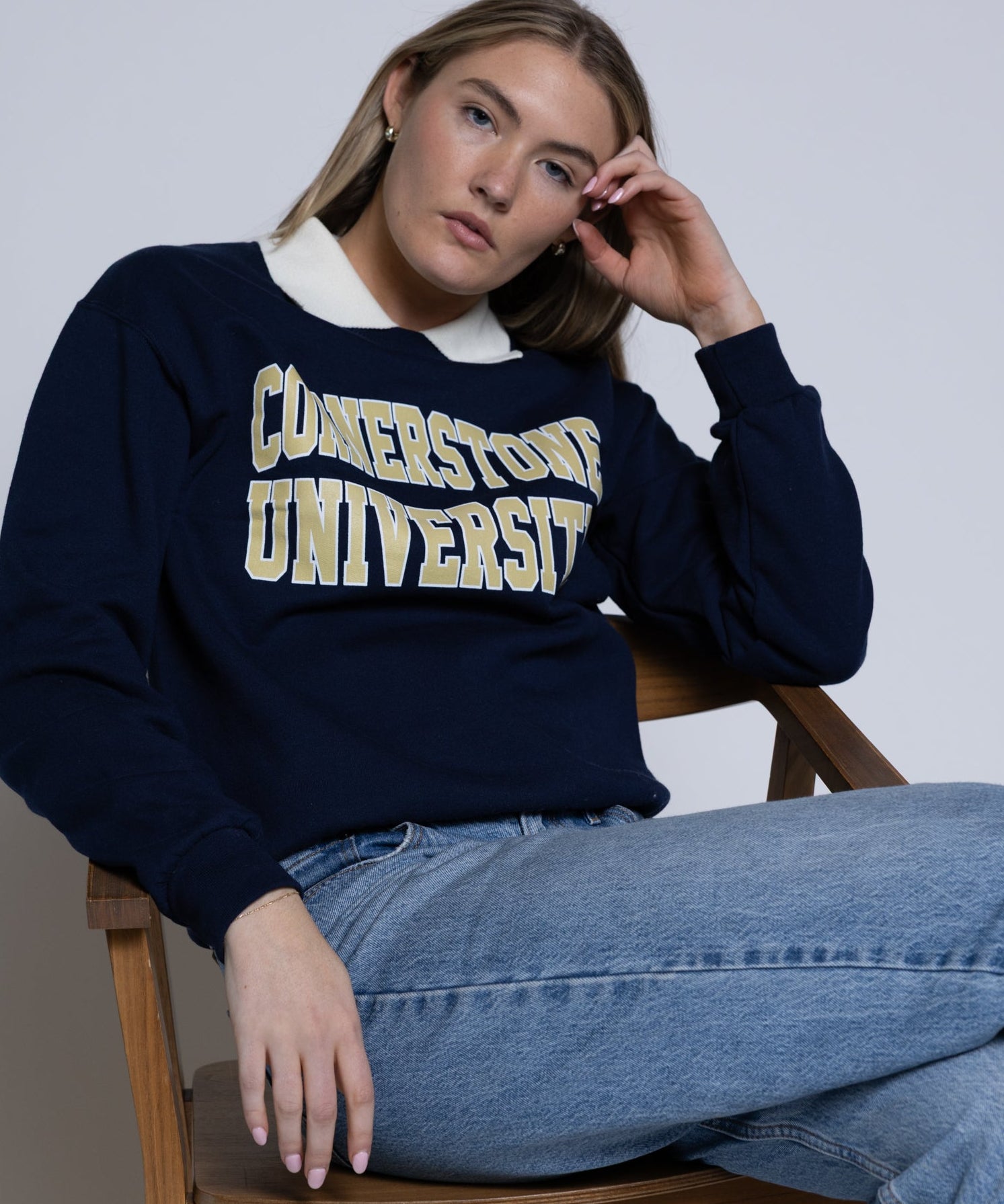 Person wearing a navy blue crewneck with 'Cornerstone University' text, sitting on a wooden chair.