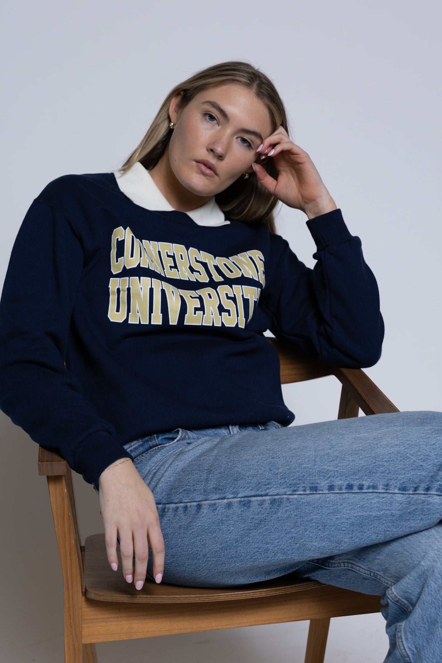 Person wearing a navy blue crewneck with 'Cornerstone University' text, sitting on a wooden chair.