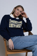Load image into Gallery viewer, Person wearing a navy blue crewneck with &#39;Cornerstone University&#39; text, sitting on a wooden chair.
