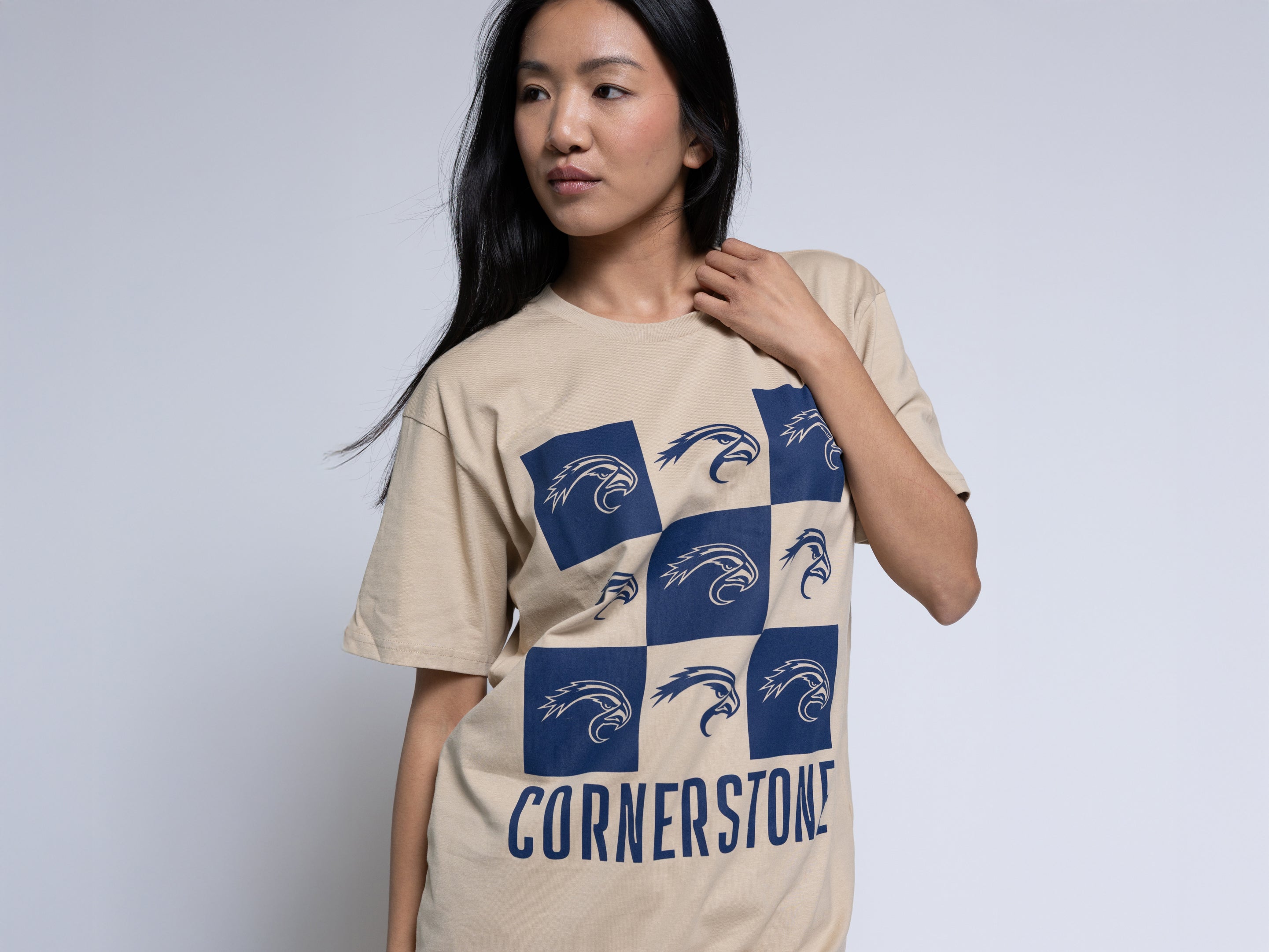 Woman wearing a beige t-shirt with a blue mascot checkered design and 'Cornerstone' text.