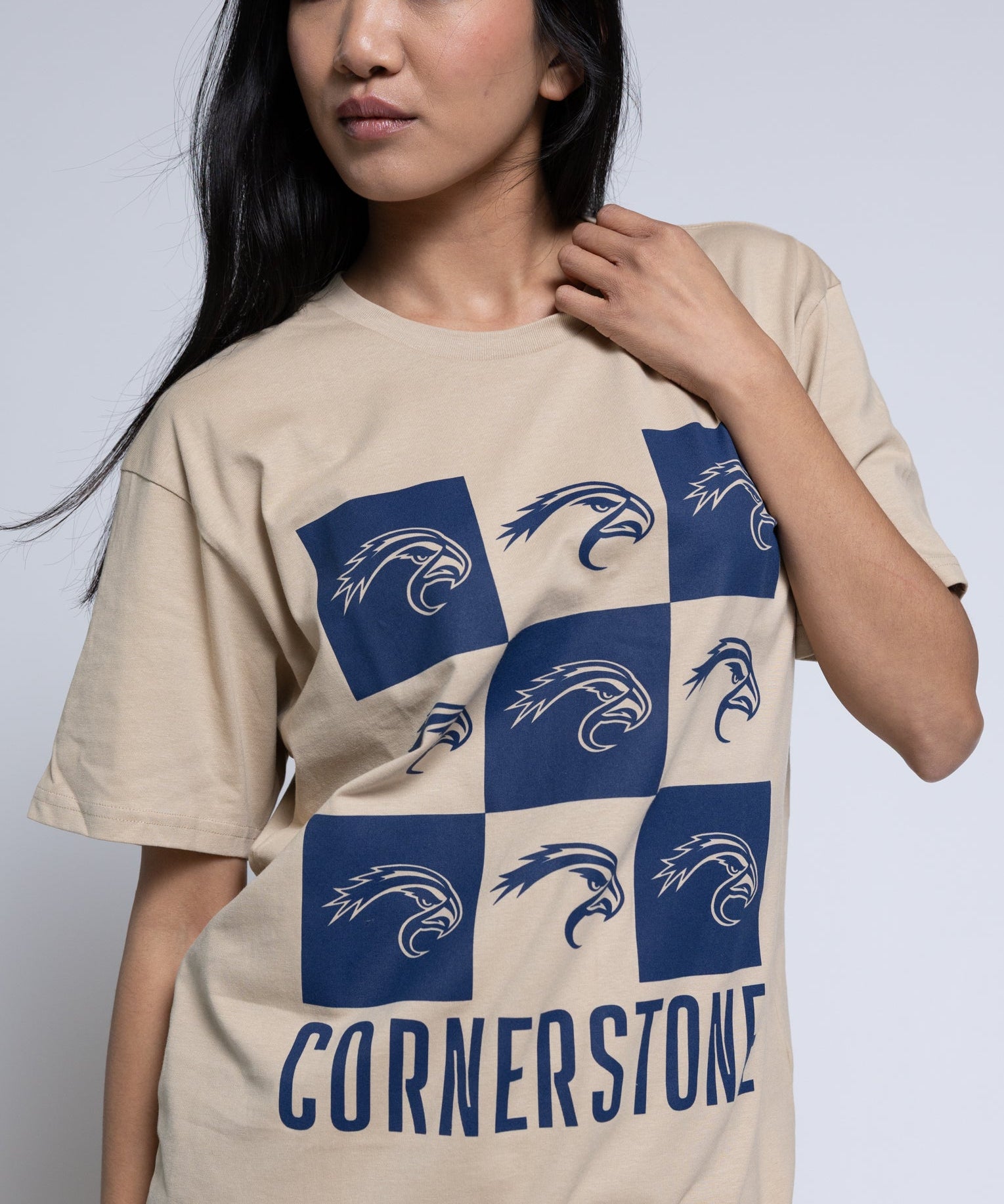 Woman wearing a beige t-shirt with a blue mascot checkered design and 'Cornerstone' text.
