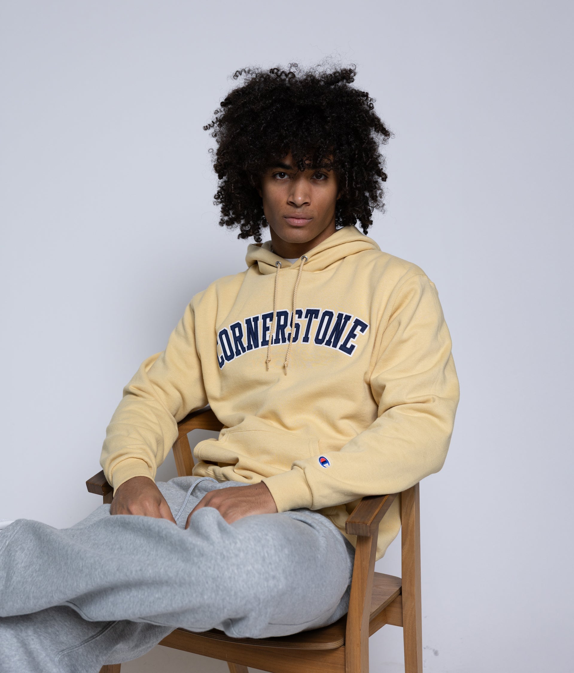 Man sitting in a wooden chair with a 'Cornerstone' hoodie on