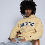 Man wearing a gold-yellow hoodie with 'Cornerstone' text sitting with a plain background behind him