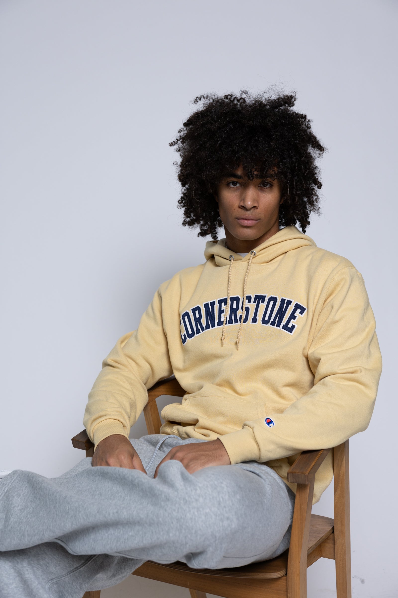 Man wearing a gold-yellow hoodie with 'Cornerstone' text sitting with a plain background behind him