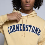 Person wearing a gold-yellow hoodie with 'Cornerstone' text on a plain background