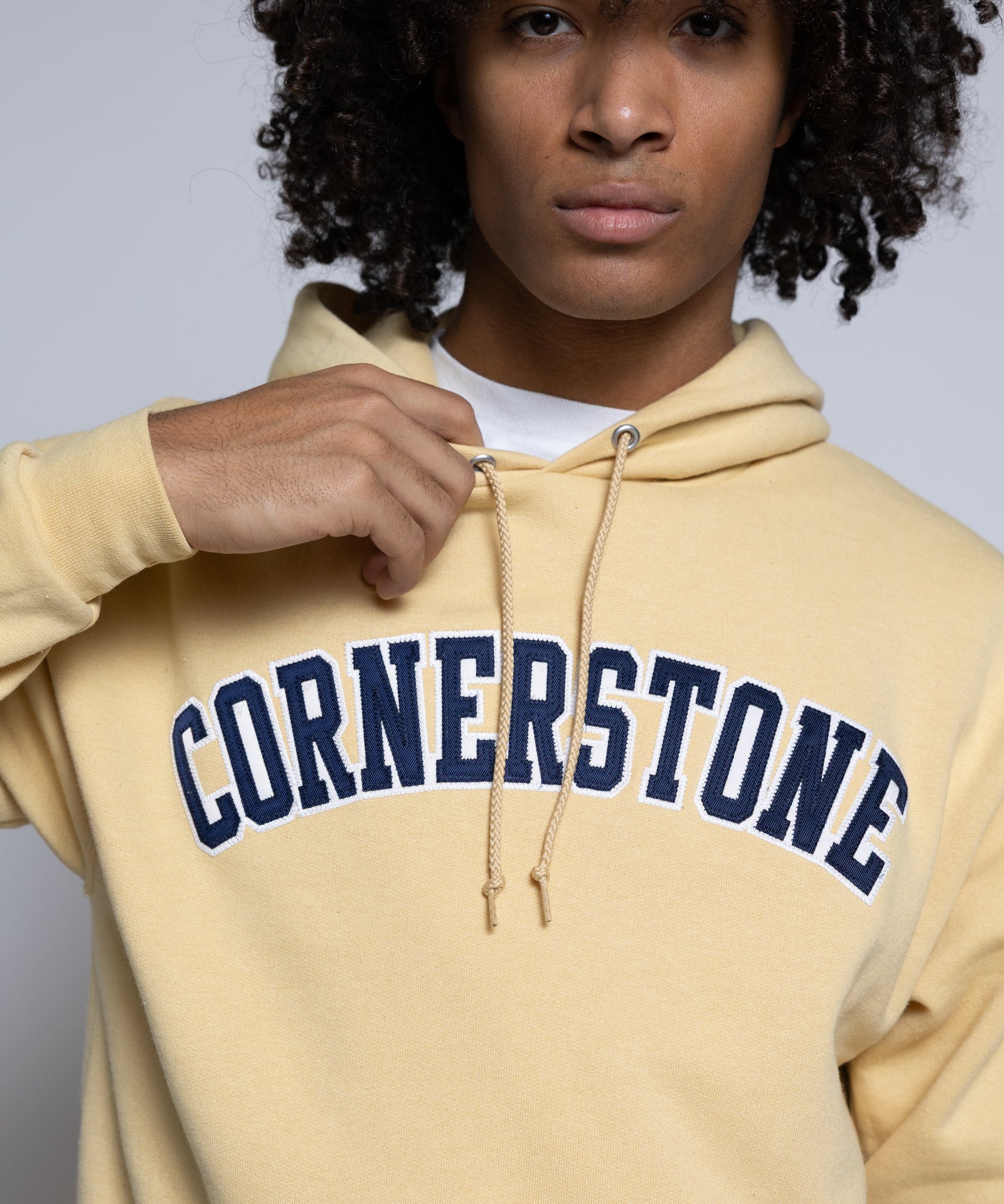 Person wearing a gold-yellow hoodie with 'Cornerstone' text on a plain background