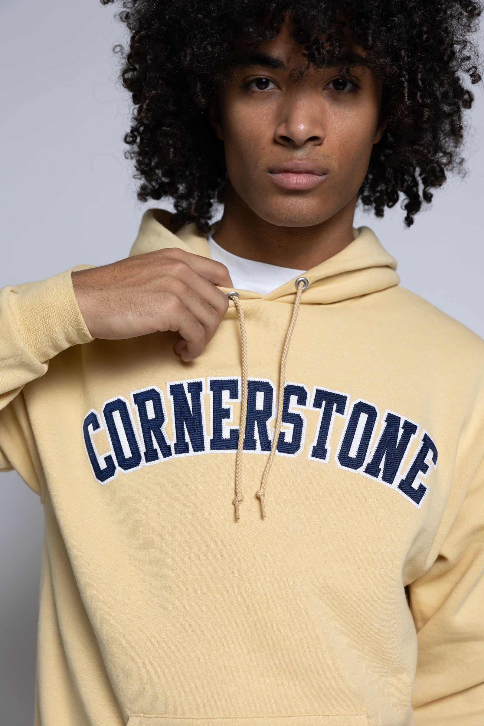 Person wearing a gold-yellow hoodie with 'Cornerstone' text on a plain background