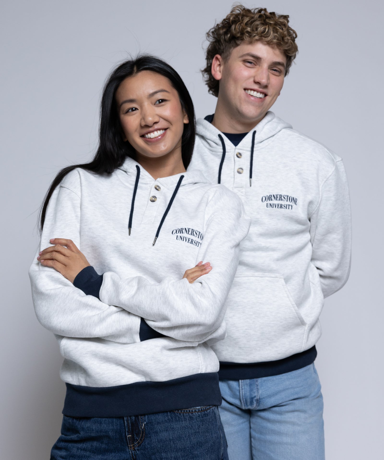 Two people wearing light hoodies with 'Cornerstone University' printed on them against a plain background
