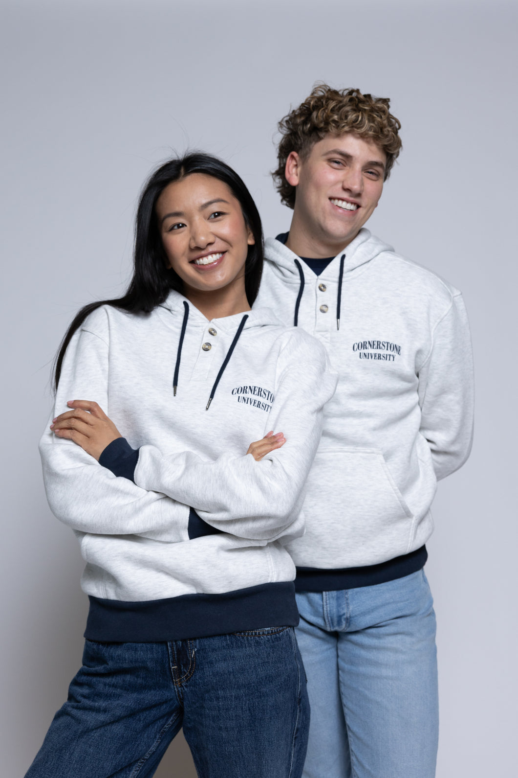 Two people wearing light hoodies with 'Cornerstone University' printed on them against a plain background