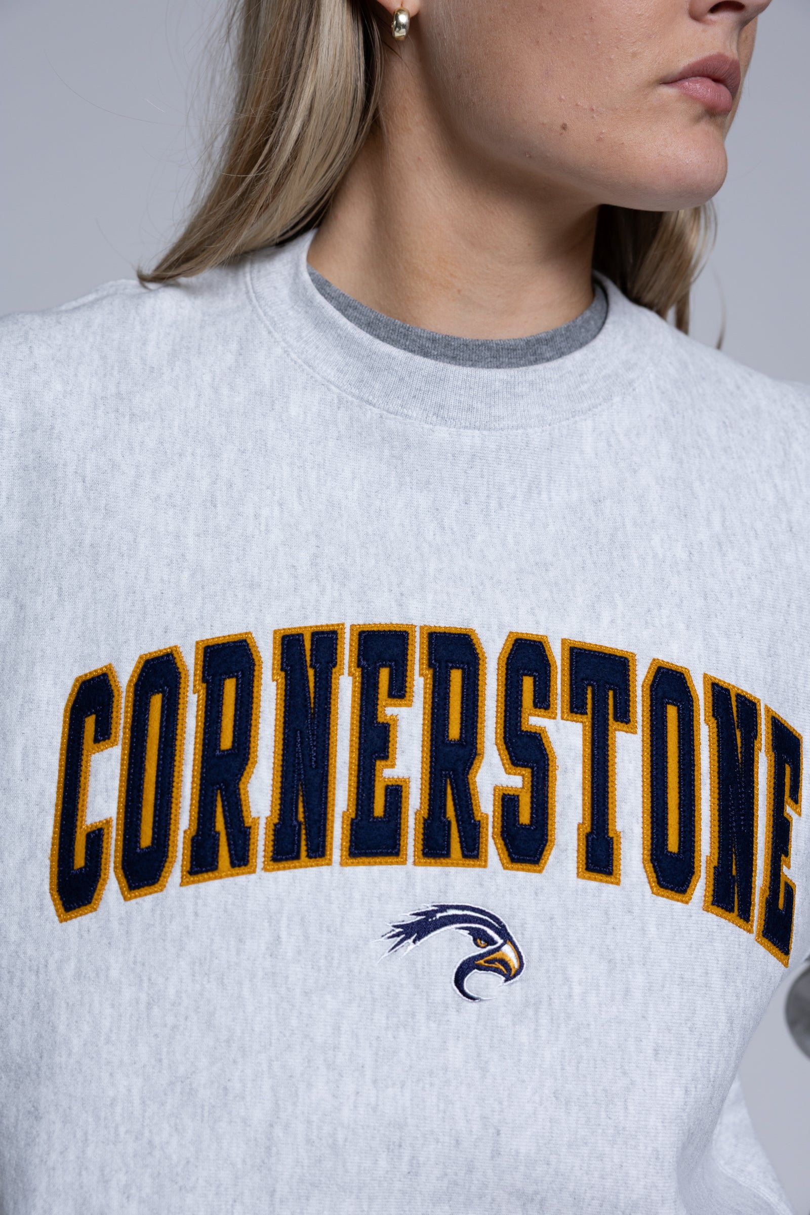 Person wearing a light crewneck sweatshirt with 'Cornerstone' on it
