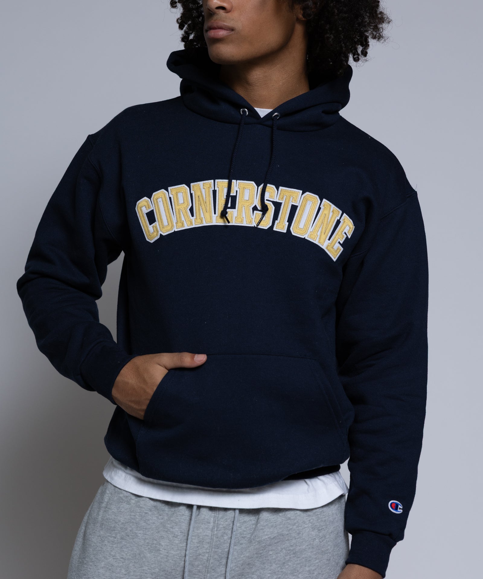Person wearing a navy hoodie with 'Cornerstone' text on a plain background
