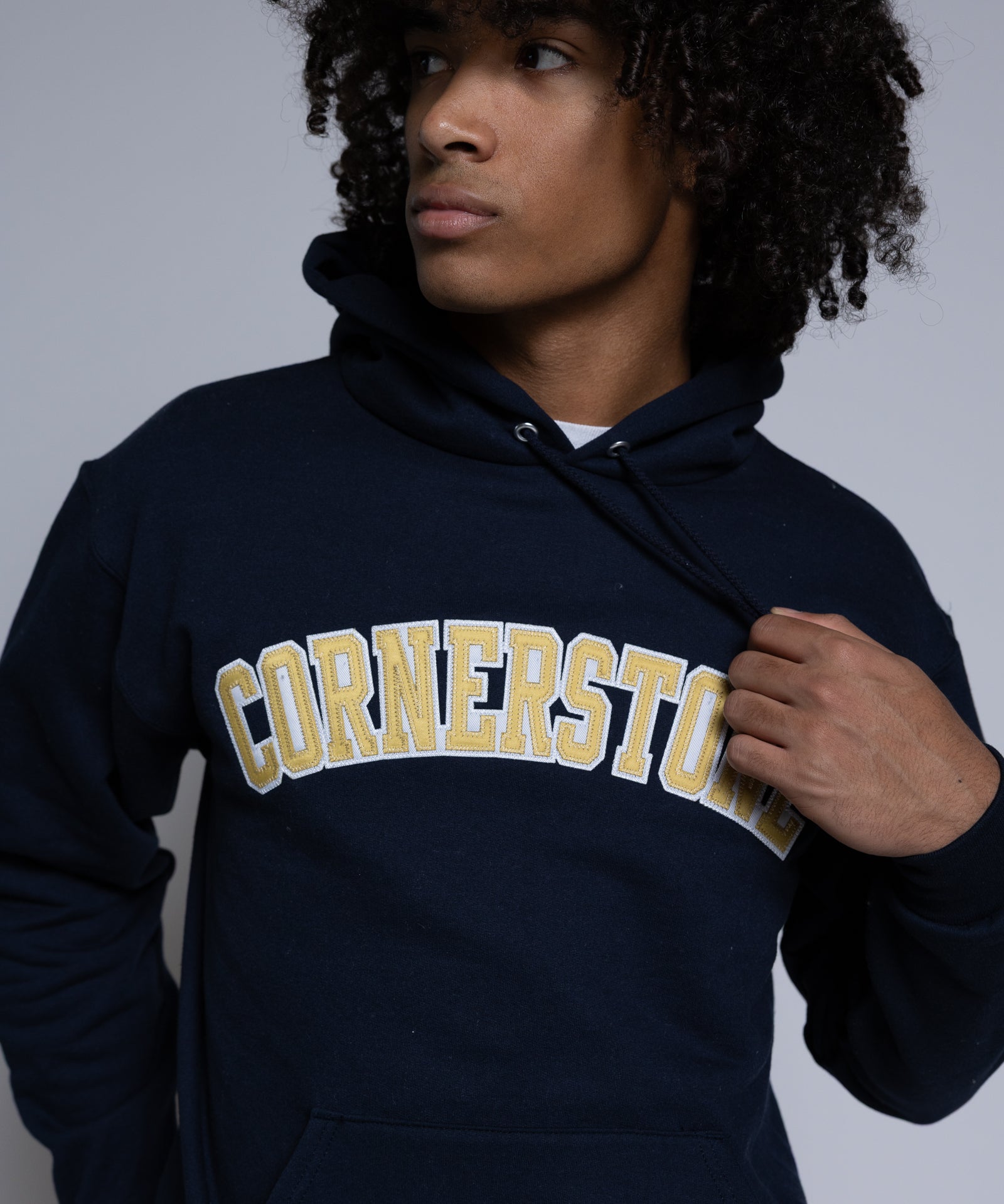Person wearing a navy hoodie with 'Cornerstone' text on a plain background
