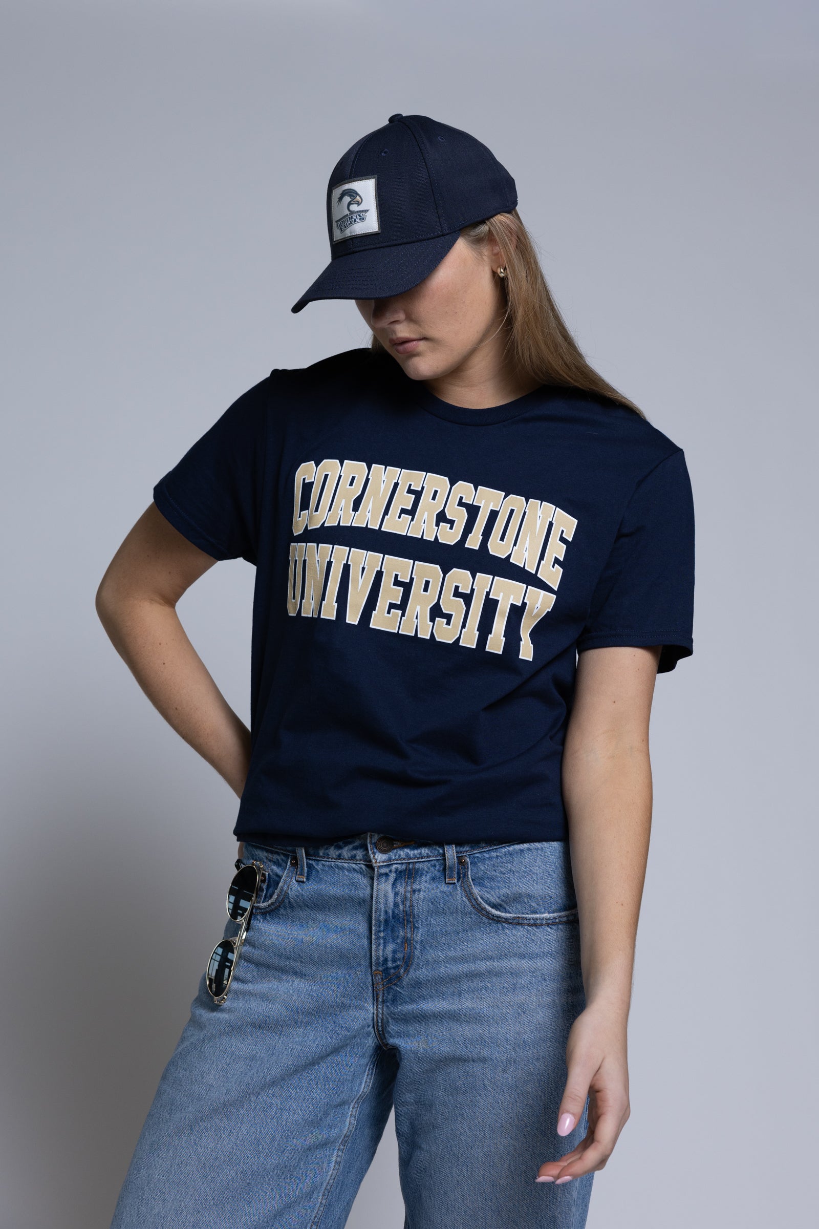 Woman wearing a navy 'Cornerstone University' t-shirt and cap on a plain background