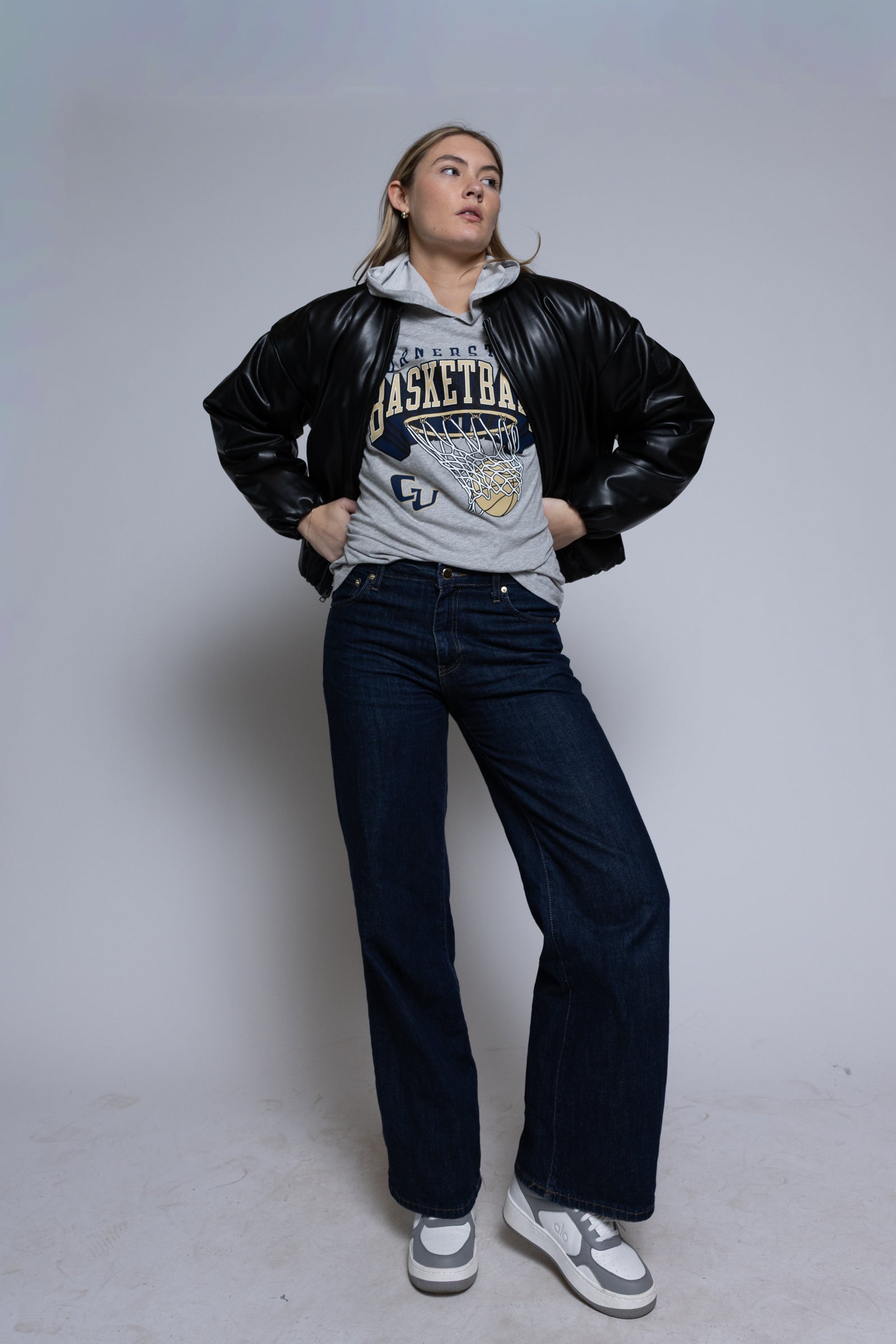 Person wearing a black leather jacket over a gray hoodie with Cornerstone basketball graphics on a plain background