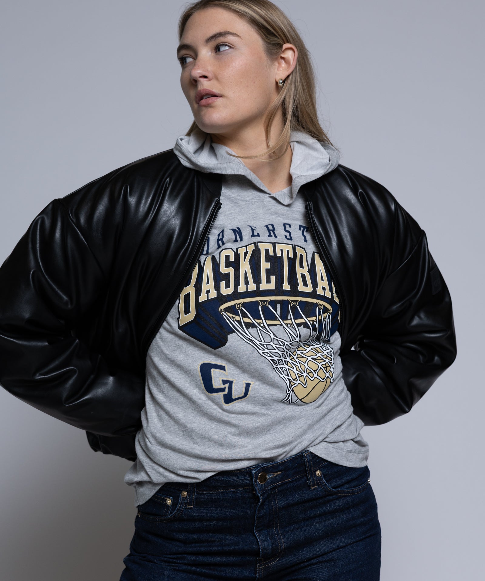 Person wearing a black leather jacket over a gray hoodie with Cornerstone basketball graphics on a plain background