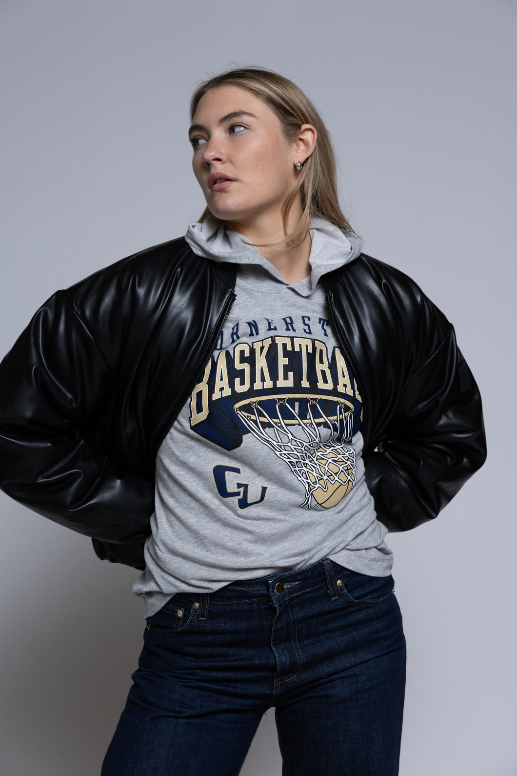 Person wearing a black leather jacket over a gray hoodie with Cornerstone basketball graphics on a plain background