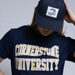 Woman wearing a navy blue t-shirt with 'Cornerstone University' text and a navy hat with a plain background behind her