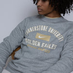 Person wearing a gray sweatshirt with 'Cornerstone University Golden Eagles Grand Rapids' text sitting on a wooden chair